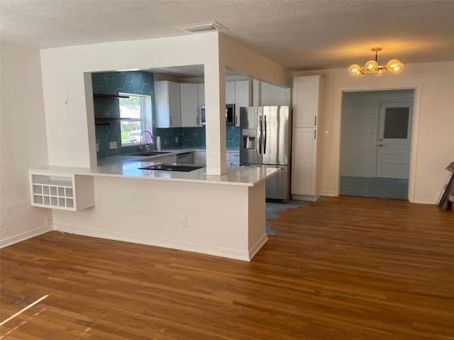 kitchen featuring dark hardwood / wood-style flooring, white cabinets, kitchen peninsula, a textured ceiling, and appliances with stainless steel finishes