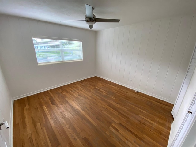 empty room with ceiling fan, wooden walls, and dark hardwood / wood-style flooring