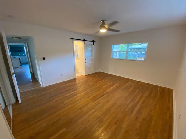 unfurnished bedroom with ceiling fan, a barn door, and hardwood / wood-style floors