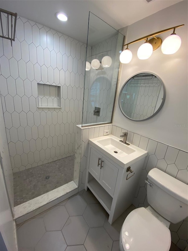 bathroom featuring tile walls, a tile shower, vanity, tile patterned floors, and toilet