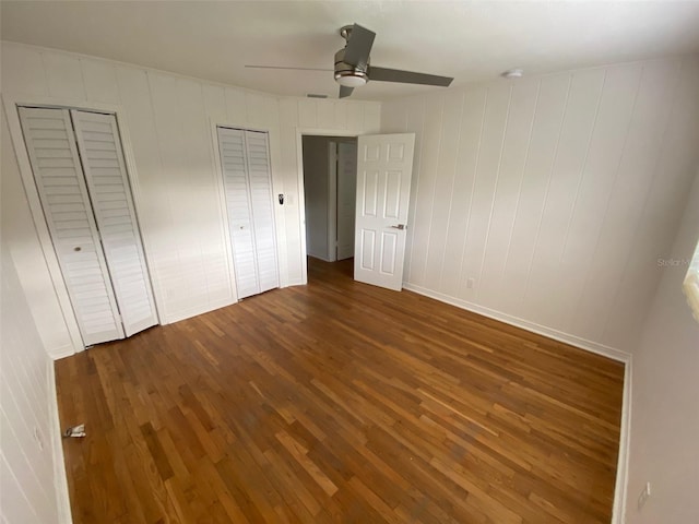 unfurnished bedroom featuring multiple closets, ceiling fan, and dark hardwood / wood-style floors