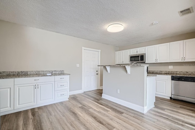 11335 Pickford St, Spring Hill, FL 34609 - kitchen featuring appliances with stainless steel finishes, white cabinetry, light wood-style flooring, light stone countertops, and a textured ceiling