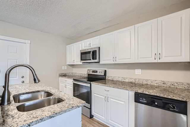 kitchen with stainless steel appliances, white cabinetry, light stone countertops, sink, and light hardwood / wood-style floors