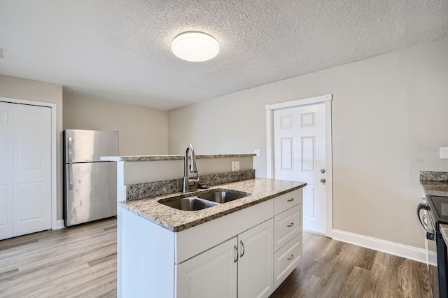 kitchen with sink, a textured ceiling, white cabinets, stainless steel fridge, and light wood-type flooring