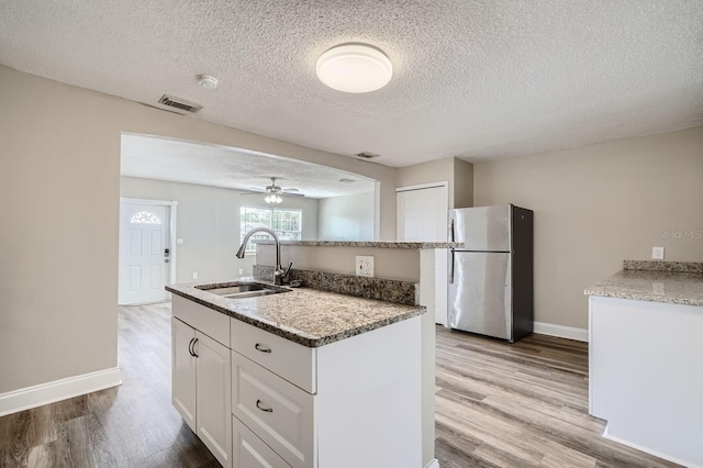 kitchen featuring stainless steel fridge, a textured ceiling, sink, white cabinets, and light hardwood / wood-style flooring