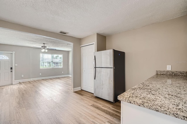 kitchen featuring a textured ceiling, stainless steel refrigerator, light stone countertops, light hardwood / wood-style floors, and ceiling fan