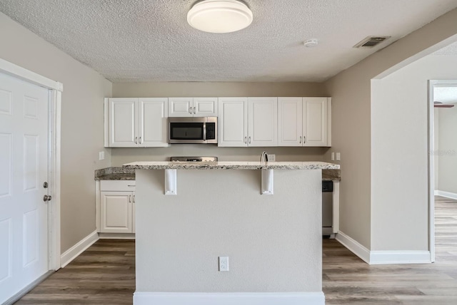 kitchen with dark wood-type flooring, white cabinetry, and an island with sink