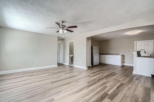 unfurnished living room featuring ceiling fan, a textured ceiling, sink, and light hardwood / wood-style flooring