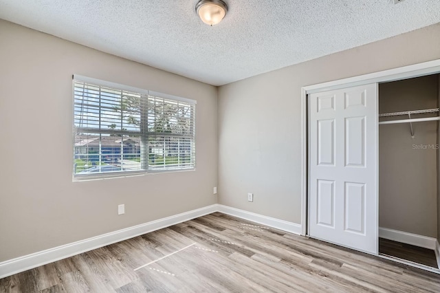 unfurnished bedroom with light hardwood / wood-style floors, a textured ceiling, and a closet