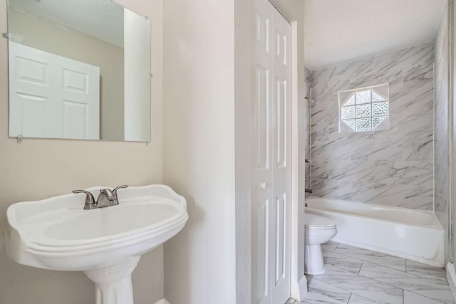 full bathroom featuring a textured ceiling, toilet, sink, and tiled shower / bath combo