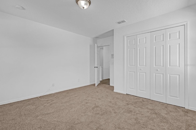 unfurnished bedroom featuring a textured ceiling, light carpet, and a closet