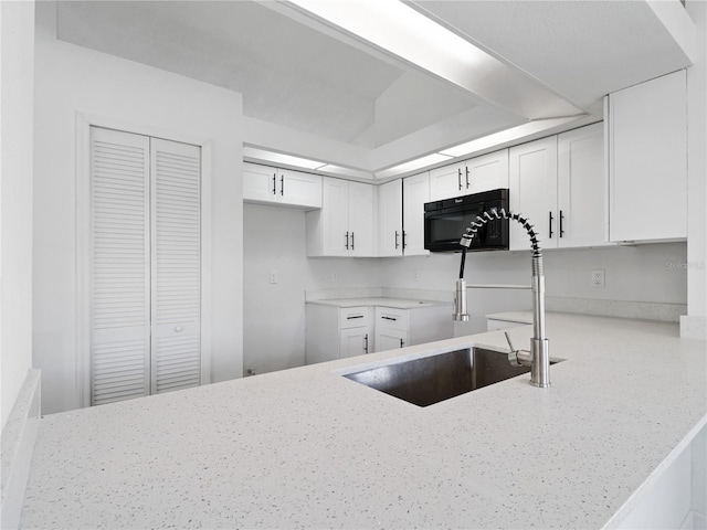 kitchen featuring white cabinetry, kitchen peninsula, sink, and light stone countertops