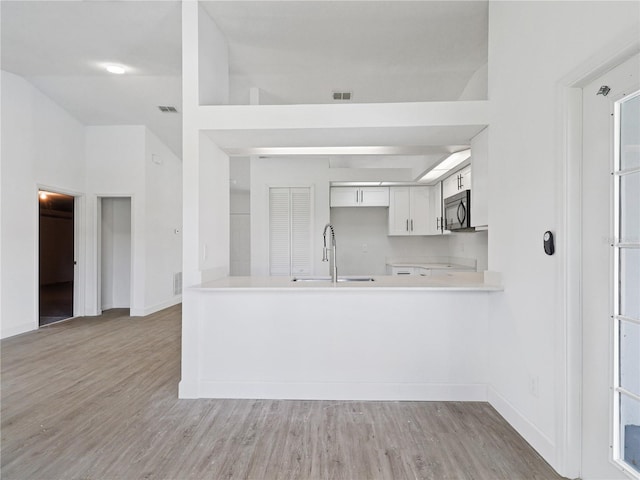 kitchen featuring white cabinetry, sink, light wood-type flooring, and kitchen peninsula