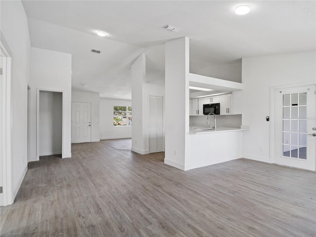 unfurnished living room featuring high vaulted ceiling, sink, and light hardwood / wood-style flooring