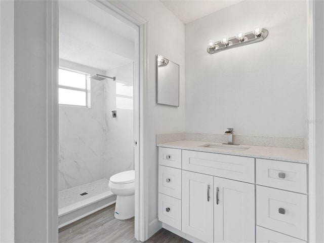 bathroom with tiled shower, wood-type flooring, toilet, and vanity