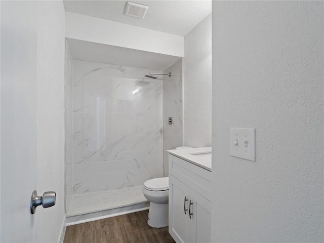 bathroom featuring toilet, vanity, hardwood / wood-style floors, and a tile shower