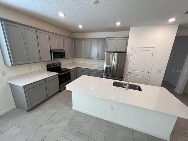 kitchen with gray cabinetry, sink, stainless steel appliances, a textured ceiling, and a kitchen island with sink