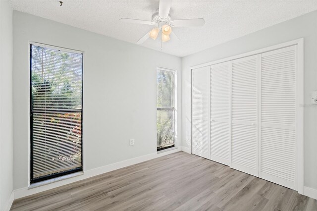 unfurnished bedroom featuring ceiling fan, a closet, a textured ceiling, and light wood-type flooring