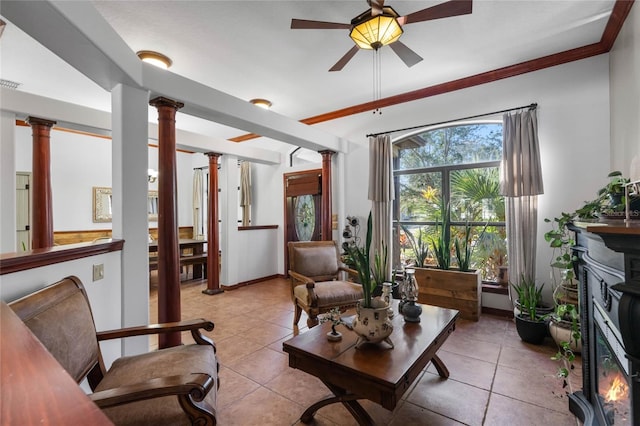 tiled living room featuring a fireplace, ceiling fan, crown molding, and decorative columns