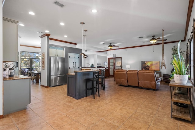 kitchen with hanging light fixtures, a kitchen island with sink, ornamental molding, light stone countertops, and stainless steel fridge