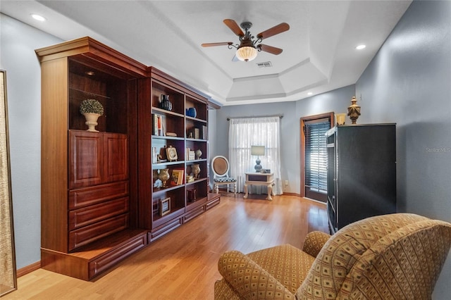 sitting room with hardwood / wood-style flooring, ceiling fan, and a tray ceiling