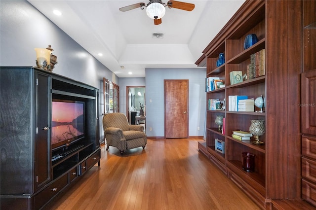 sitting room with hardwood / wood-style floors, ceiling fan, and a raised ceiling