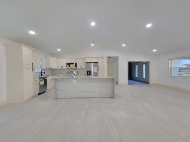 kitchen featuring stainless steel appliances, vaulted ceiling, sink, a kitchen island, and light stone countertops