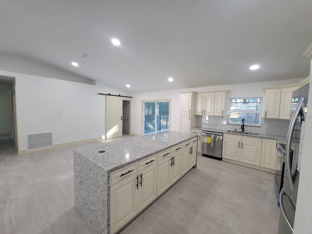 kitchen with light stone counters, stainless steel appliances, a barn door, sink, and lofted ceiling