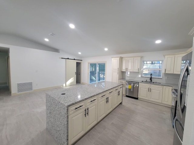 kitchen featuring light stone counters, stainless steel appliances, a barn door, sink, and vaulted ceiling