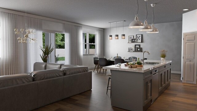 kitchen featuring sink, a textured ceiling, decorative light fixtures, an island with sink, and dark wood-type flooring