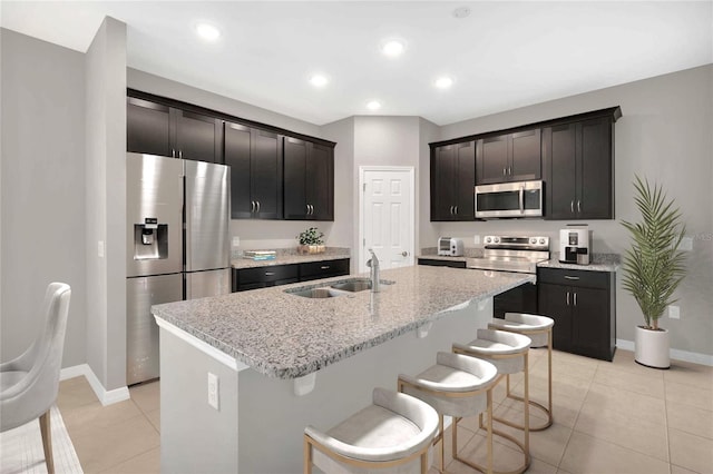 kitchen with a kitchen island with sink, appliances with stainless steel finishes, light tile patterned floors, and light stone counters