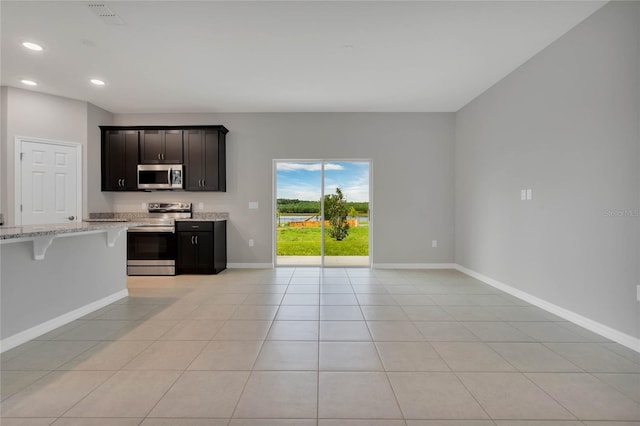 kitchen featuring a kitchen breakfast bar, stainless steel appliances, light tile patterned floors, and light stone countertops