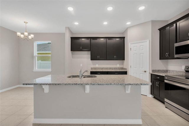 kitchen featuring stainless steel appliances, light stone counters, a notable chandelier, sink, and an island with sink