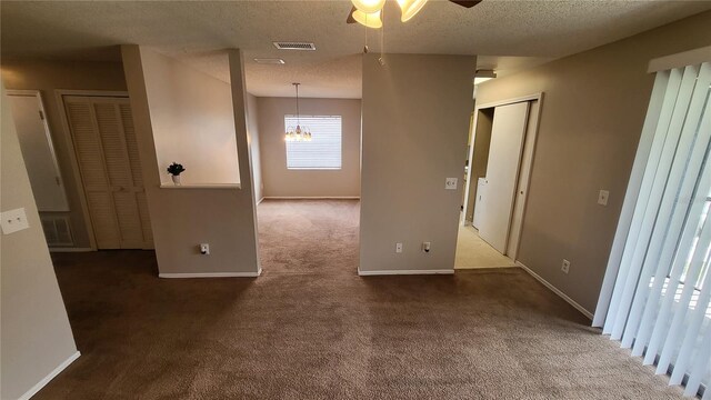 carpeted spare room featuring a textured ceiling and ceiling fan with notable chandelier