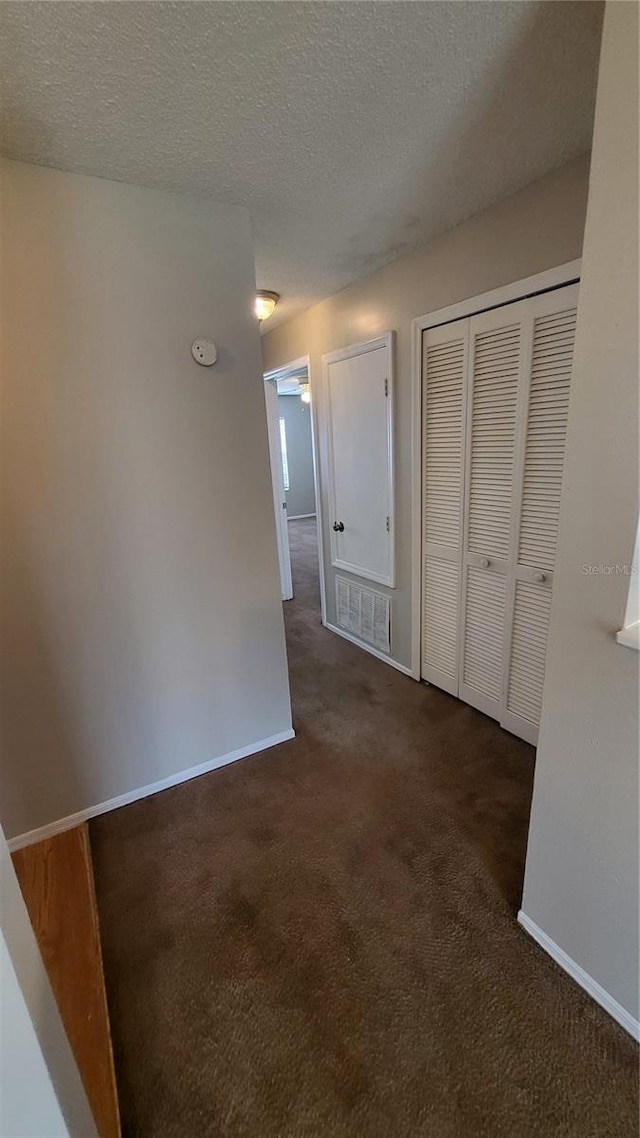 interior space featuring a textured ceiling and dark carpet