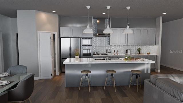 kitchen with tasteful backsplash, pendant lighting, an island with sink, dark wood-type flooring, and wall chimney exhaust hood