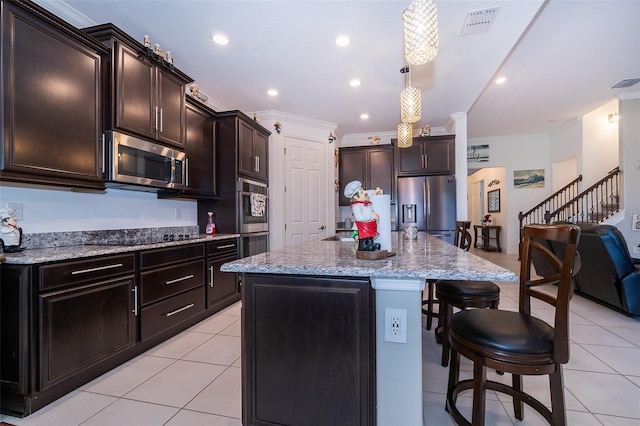 kitchen with an island with sink, hanging light fixtures, appliances with stainless steel finishes, and ornamental molding