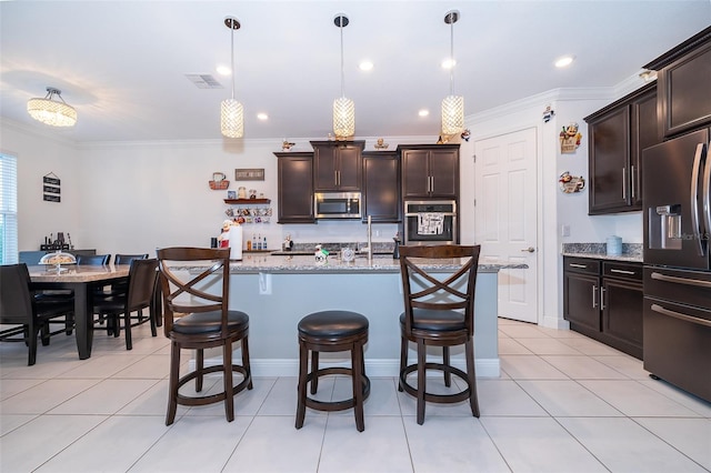 kitchen with dark brown cabinetry, light stone counters, appliances with stainless steel finishes, hanging light fixtures, and an island with sink