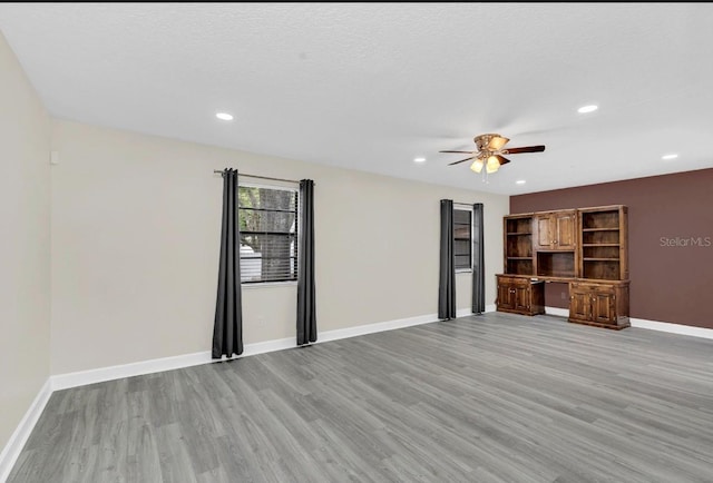 unfurnished living room with a textured ceiling, built in desk, light hardwood / wood-style flooring, and ceiling fan