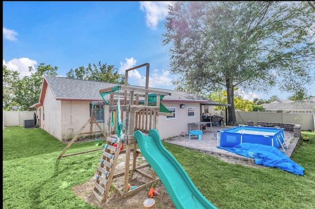 view of playground featuring a yard, a covered pool, and central air condition unit