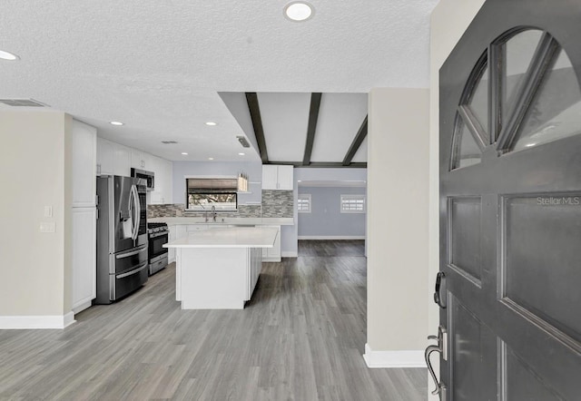 kitchen with pendant lighting, white cabinets, light hardwood / wood-style floors, a kitchen island, and stainless steel appliances