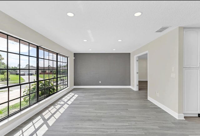 unfurnished room with a textured ceiling, light hardwood / wood-style floors, and a healthy amount of sunlight