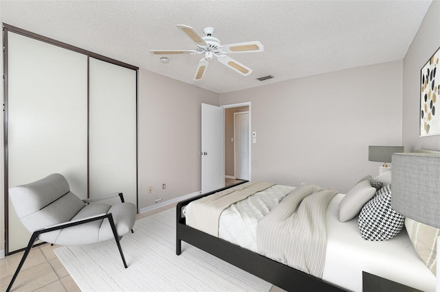 tiled bedroom with a closet, a textured ceiling, and ceiling fan