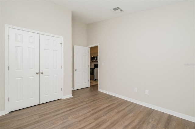 unfurnished bedroom with a closet, light wood-type flooring, and a towering ceiling