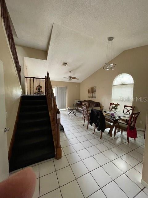 dining space with light tile patterned floors, lofted ceiling, visible vents, stairway, and a textured ceiling