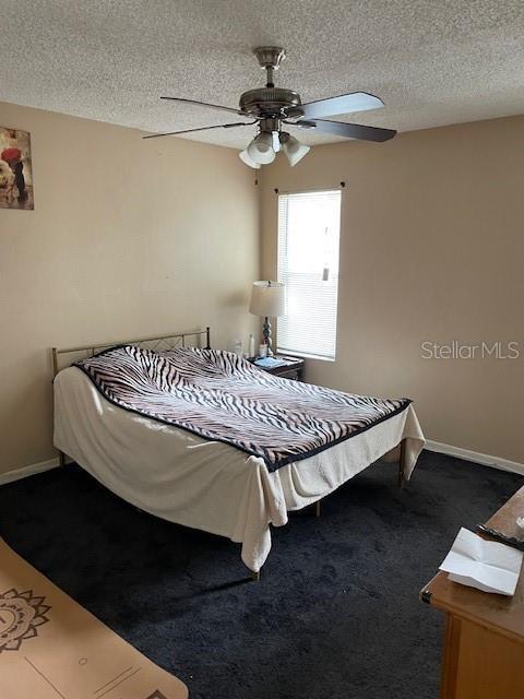 bedroom with ceiling fan, baseboards, a textured ceiling, and carpet flooring