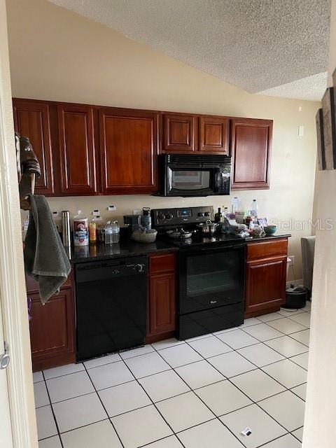 kitchen featuring dark countertops, black appliances, light tile patterned floors, and vaulted ceiling