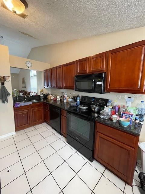 kitchen with dark countertops, lofted ceiling, light tile patterned flooring, a sink, and black appliances