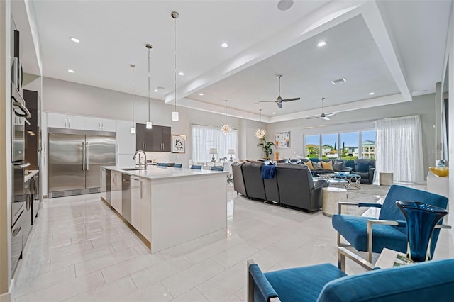 kitchen featuring stainless steel built in fridge, white cabinets, hanging light fixtures, sink, and a kitchen island with sink