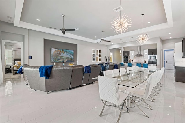 dining space with a tray ceiling, light tile patterned floors, and ceiling fan with notable chandelier